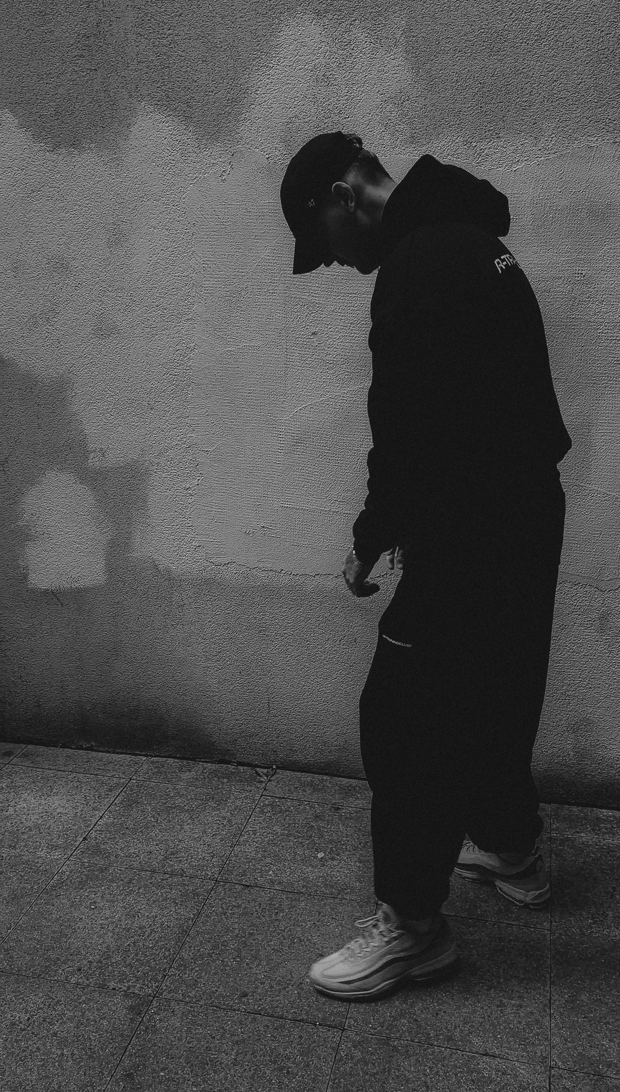 Person wearing a hoodie and pants against a textured wall.