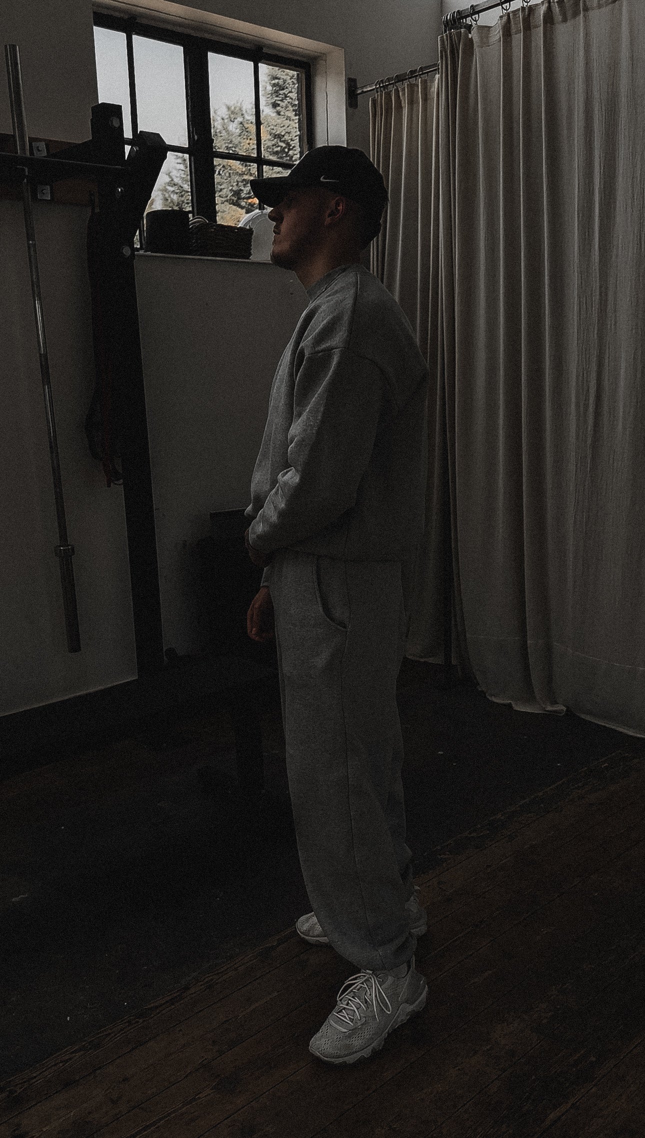 Person standing in a dimly lit room with curtains and a window.