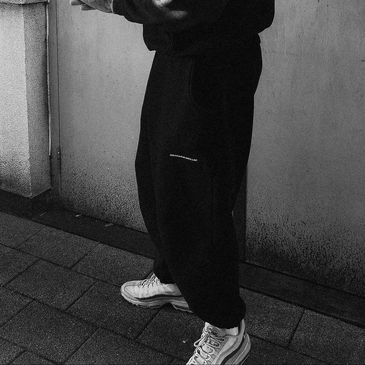 Man in black outfit standing against a plain wall