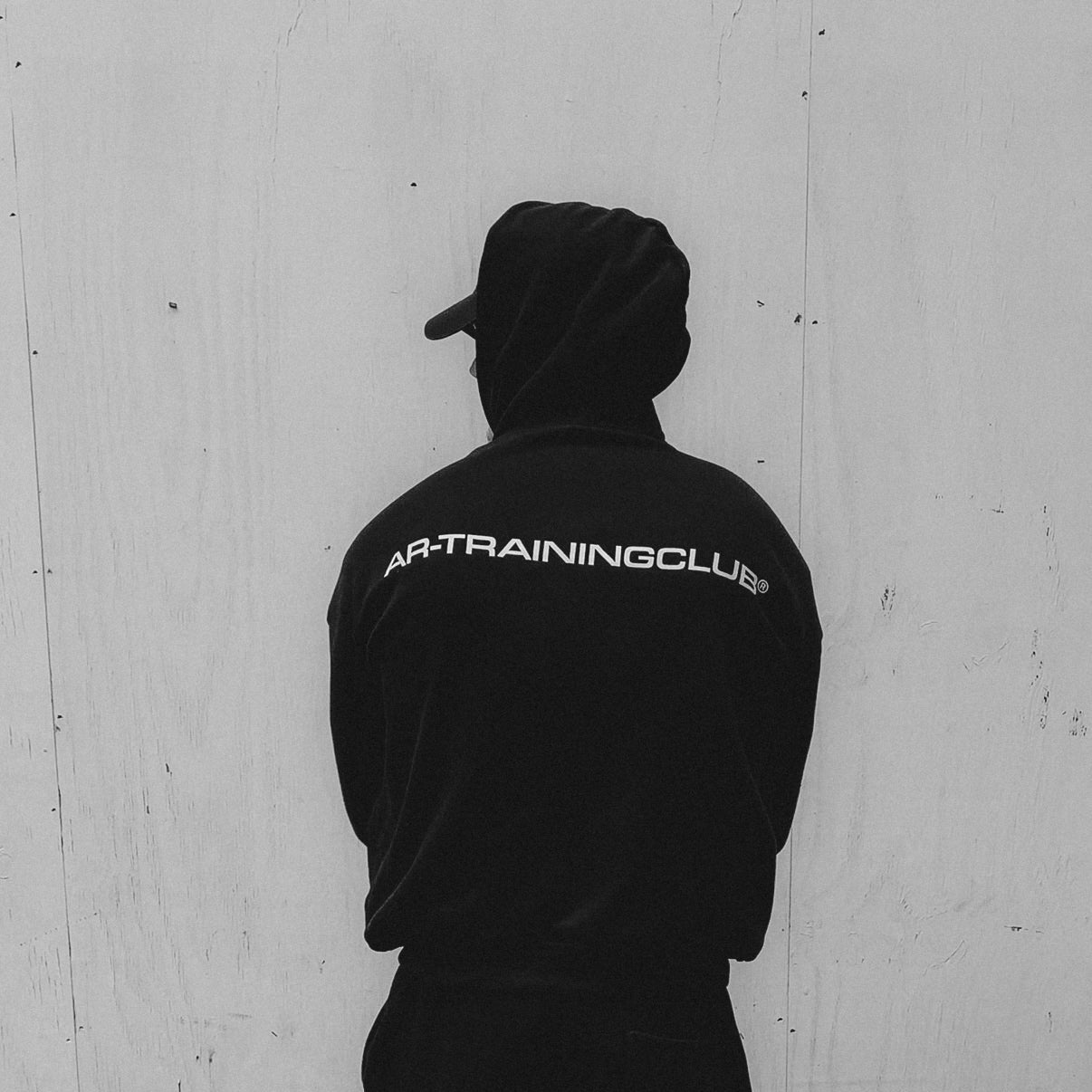 Person wearing a black tracksuit with 'Kap Training Club' branding against a light-colored wall.